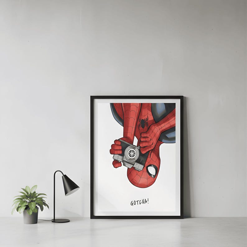 May include: Framed art print featuring a comic-style illustration of Spider-Man holding a camera. The superhero is depicted in his classic red and blue suit, with the word "GOTCHA!" below the image. The artwork is set against a white background.