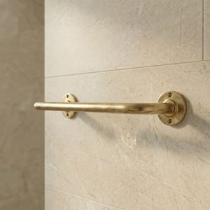May include: A brass-colored towel bar mounted on a light beige tiled wall. The bar is cylindrical with circular mounting plates on each end, each with three screw holes. The finish has a slightly aged appearance.