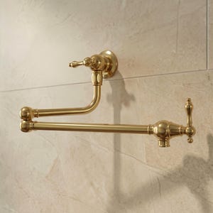 May include: A wall-mounted pot filler faucet with a polished brass finish. This articulated kitchen fixture features two swing arms with swivel joints, a single lever handle at the base, and a vertical handle at the nozzle end for water control.