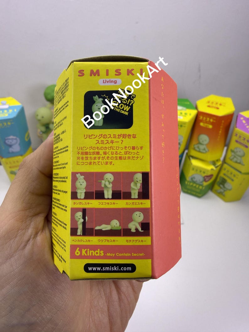 A hand holding a yellow box with a picture of a living toy, surrounded by other similar boxes.