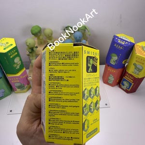 A hand holding a yellow box with text and illustrations, with other colorful boxes visible in the background.