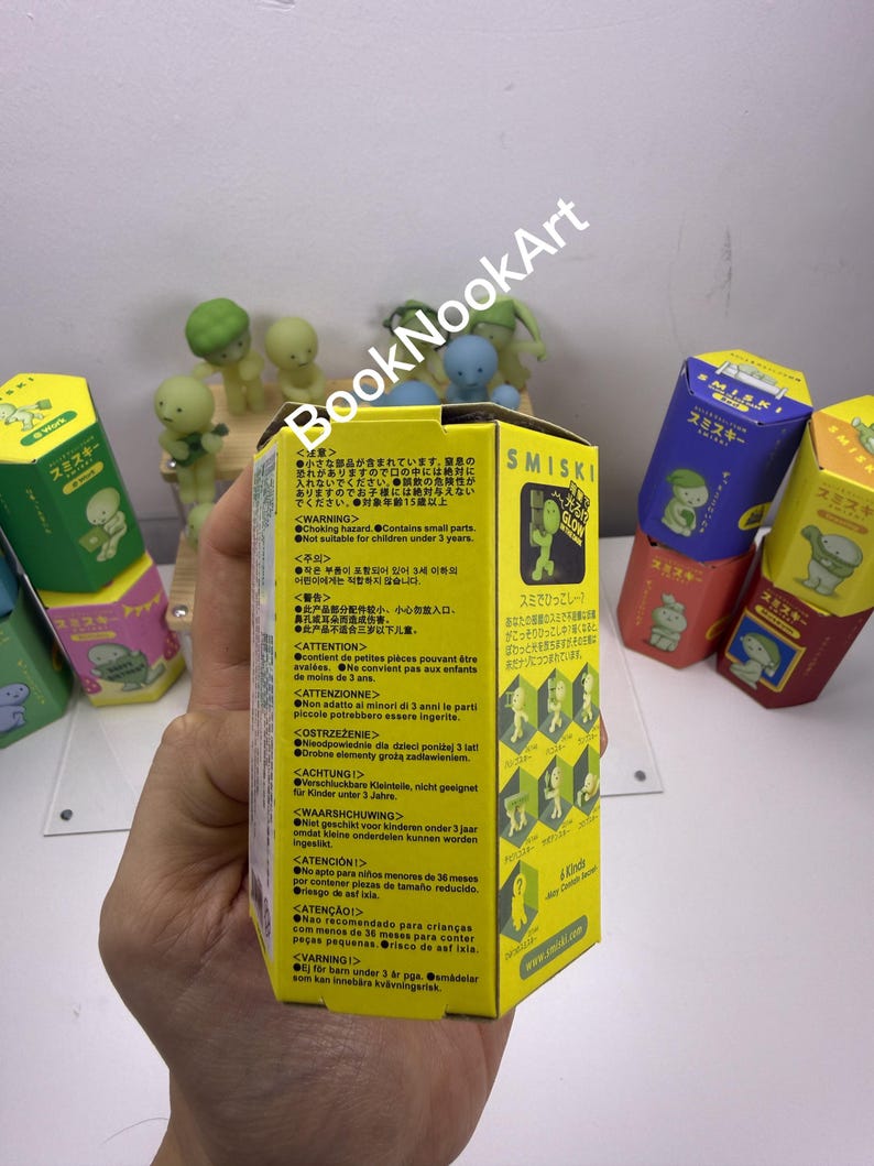 A hand holding a yellow box with text and illustrations, with other colorful boxes visible in the background.