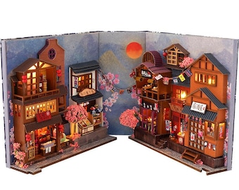 Puede incluir: Diorama en miniatura de un pueblo japonés con edificios de madera detallados, ventanas iluminadas y detalles de flores de cerezo. La escena incluye un fondo de puesta de sol y cielo nocturno, creando una exhibición encantadora y detallada.