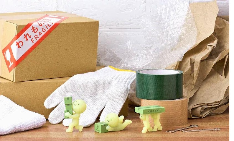 a variety of objects, including a cardboard box, a white glove, a green tape roll, and several small figurines, all arranged on a wooden surface.