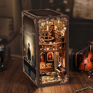 Puede incluir: Un rincón de libro de madera marrón detallado con una escena interior en miniatura. La escena incluye un piano, un violín y una figura en un balcón. El rincón del libro tiene el texto "A Mystery Case Involving A Hidden Box" en el lateral.