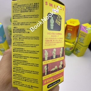 A hand holding a yellow box with text and images, including a small figurine and various safety warnings.