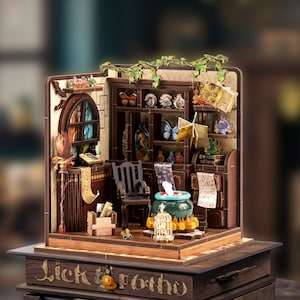 Può includere: Diorama in miniatura in legno di uno studio di mago, con una libreria con farfalle e bottiglie di pozioni, un calderone e una vetrata. La base recita "Lick Brotho".