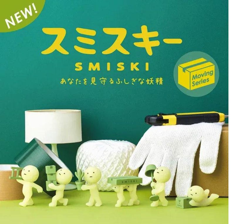 a collection of small figurines, including a group of people and a hand, arranged on a green surface. The figurines are illuminated in a yellowish hue, creating a visually striking contrast against the green background. The text "SMISKI" is prominently displayed in the center of the image, and there is a logo for the "MOVING SERIES" in the top right corner.