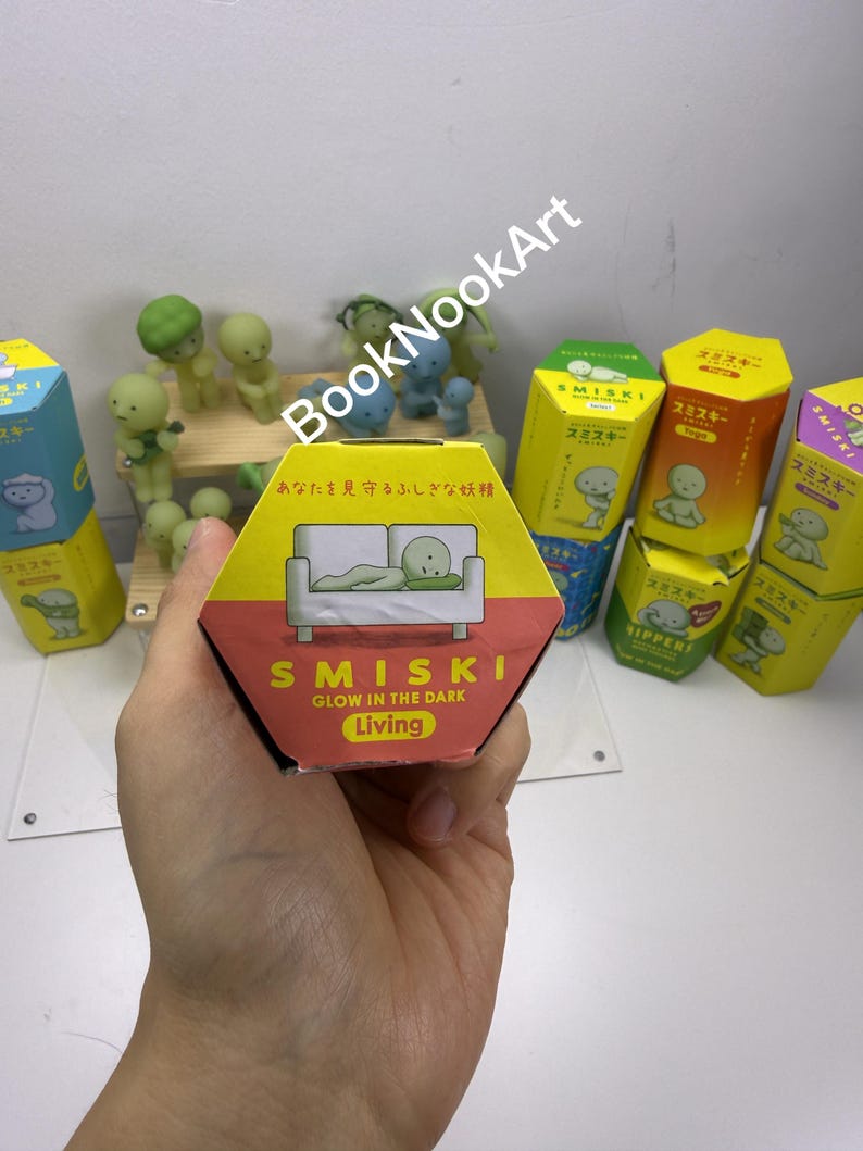 A hand holding a hexagonal box with a cartoon image of a green frog on it, surrounded by various colorful boxes and figurines.
