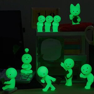 A collection of small, glowing green figurines arranged on a desk, with some of them holding objects like a laptop and a keyboard.