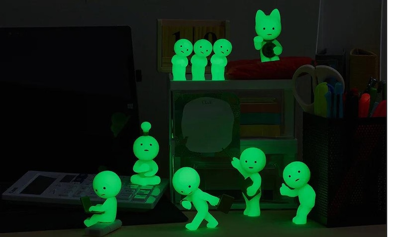 A collection of small, glowing green figurines arranged on a desk, with some of them holding objects like a laptop and a keyboard.