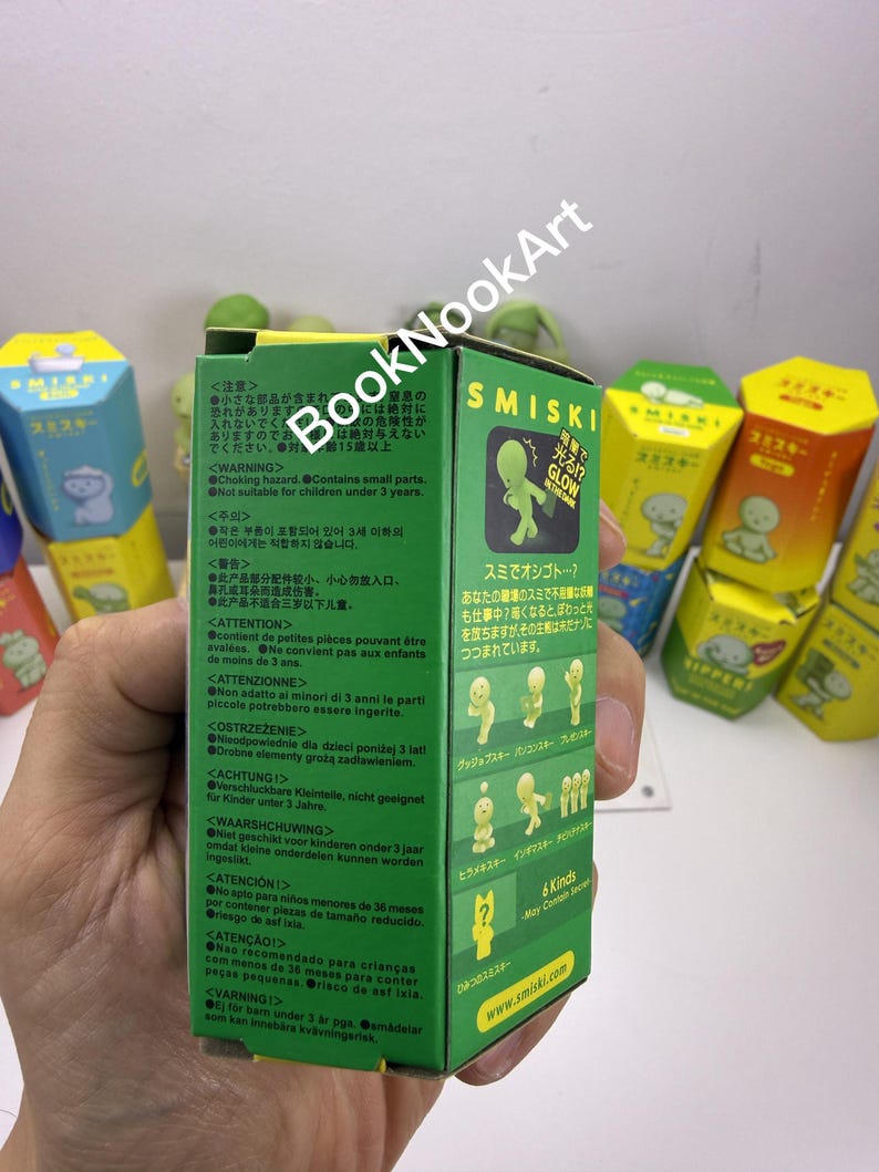 A person's hand holding a green box with text and illustrations, with colorful boxes in the background.