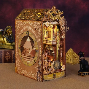 Könnte beinhalten: Detailliertes, beleuchtetes Holzmodell einer altägyptischen Szene. Das Modell zeigt aufwendige Ausschnitte, eine Pyramide und den Text "Exploring the Mysterious City". Die Farbpalette umfasst Gold, Braun und Beige.