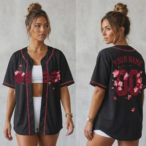 May include: Black baseball jersey with red floral and glitter accents. The front features the word "GIRL" in red glitter, and the back has "YOUR NAME" above the number "00" with floral embellishments. The jersey has a button-up front and short sleeves.