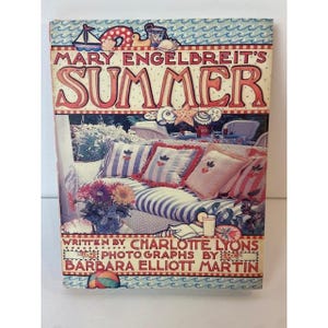 May include: A hardcover book titled Mary Engelbreit's Summer, written by Charlotte Lyons and photographed by Barbara Elliott Martin. The cover features a blue and white wave border, illustrations of beach items, and a photo of a porch with striped cushions.