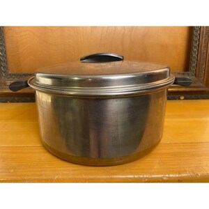 May include: A stainless steel cooking pot with a matching lid. The pot features a cylindrical body with a polished metallic finish and two black plastic handles on opposite sides. The lid is also stainless steel with a black plastic handle.