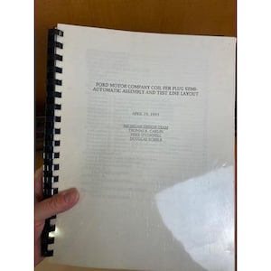 May include: A white spiral-bound technical report titled FORD MOTOR COMPANY COIL PER PLUG SEMI-AUTOMATIC ASSEMBLY AND TEST LINE LAYOUT, dated APRIL 19, 1993, listing the MICHIGAN DESIGN TEAM, THOMAS K. CARLIN, MIKE O'CONNELL, and DOUGLAS SCHELB.