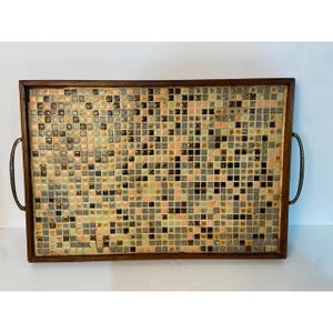 May include: A rectangular wooden serving tray featuring a mosaic surface composed of small square tiles in shades of pink, black, cream, and grey. The tray is framed by a dark wood border and includes two curved metal handles on the sides.