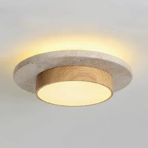 Puede incluir: Una moderna lámpara de techo con un diseño circular. Cuenta con un anillo exterior texturizado de color claro, una sección media de madera y una fuente de luz redonda y brillante. La lámpara está montada en un techo blanco.