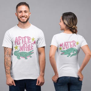 Puede incluir: Camisetas blancas con un diseño de cocodrilo de dibujos animados. Una camiseta dice "AFTER WHILE" en letras rosas de burbujas, la otra dice "LATER". Ambas camisetas tienen un gráfico de cocodrilo verde con detalles en rosa y estrellas amarillas.