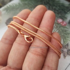 May include: Rose gold chain necklace with a lobster clasp. The chain features a tightly woven, textured design. The necklace is displayed against a neutral background, highlighting its colour and detail.