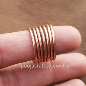 Op de afbeelding: Een stapel koperkleurige ringen op een vinger. De ringen zijn dun en hebben een glanzende afwerking. De tekst "poojacraftedjewelry" is zichtbaar aan de basis van de vinger. De ringen lijken handgemaakt.