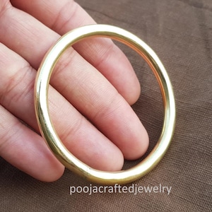 May include: A gold-colored bangle bracelet. The circular bracelet is smooth and shiny, reflecting light. The text "poojacraftedjewelry" is visible at the bottom of the image.