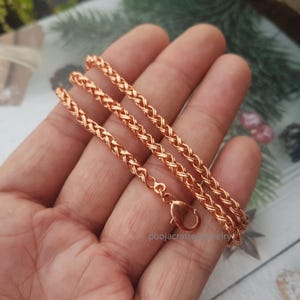 Puede incluir: Un collar de cadena de trigo en oro rosa. El collar presenta un diseño tejido y un cierre de mosquetón. La joya se exhibe sobre una superficie de color claro. El collar mide aproximadamente 45 cm de largo.