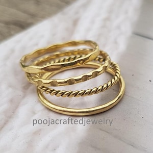 May include: Four gold rings with varied textures are stacked together. One ring has a hammered finish, another features small dots, and a third has a twisted rope pattern. The rings are displayed on a white surface. The text "poojacraftedjewelry" is visible.