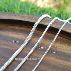 May include: Three silver chain necklaces of varying thicknesses: 1 mm, 2 mm, and 3 mm. The chains are displayed on a wooden surface with the measurements labeled. The brand name "poojacraftedjewelry" is visible.