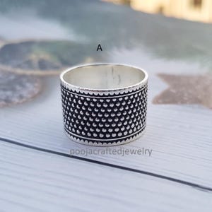 May include: A silver ring with a textured design of small, evenly spaced dots. The ring has a wide band and a decorative edge. The text "poojacraftedjewelry" is visible at the bottom of the image.