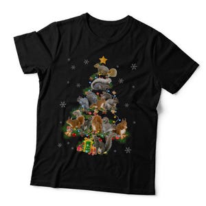 May include: A black short-sleeved t-shirt featuring a graphic of a Christmas tree formed by multiple squirrels. The tree is decorated with colourful string lights, a yellow star topper, and white snowflakes, with wrapped gifts at the base.
