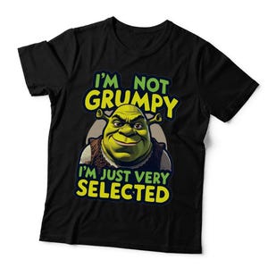 May include: A black short-sleeved t-shirt featuring a graphic of the character Shrek. The text above the character reads I'M NOT GRUMPY and the text below reads I'M JUST VERY SELECTED in bright yellow and green lettering against a dark background.