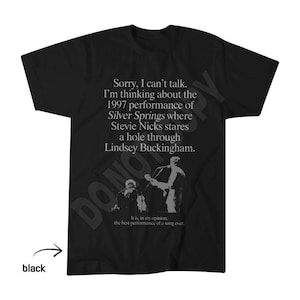 May include: A black short-sleeved t-shirt featuring white text that reads: Sorry, I can't talk. I'm thinking about the 1997 performance of Silver Springs where Stevie Nicks stares a hole through Lindsey Buckingham. It is, in my opinion, the best performance of a song ever. Below the text is a monochromatic graphic of two musicians performing on stage.