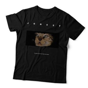 May include: A black short-sleeved t-shirt featuring the white text J O N E S Y at the top. Below the text is a rectangular graphic of a cat face emerging from darkness. Underneath the graphic is the small white text In space no one can hear you meow.