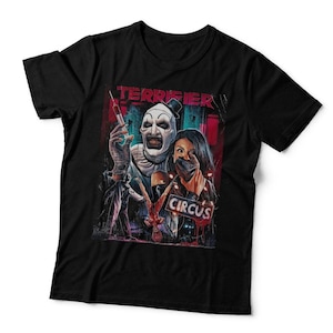 May include: A black short-sleeved t-shirt featuring a graphic print of a clown character holding a syringe, a person with a hand over their mouth, and the text TERRIFIER and CIRCUS. The design uses red, white, and blue accents on a dark background.