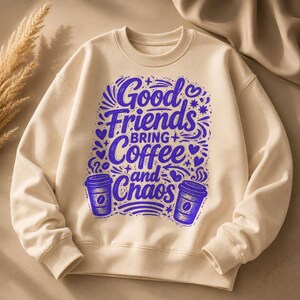 May include: Cream-colored sweatshirt with the phrase "Good Friends Bring Coffee and Chaos" in blue script. The design includes coffee cup illustrations and decorative elements. The sweatshirt has a crew neck and long sleeves.