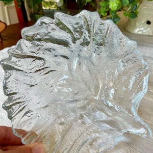 May include: A clear glass dish shaped like a large leaf with a textured, uneven surface that mimics natural veins and organic contours. The glass is transparent and features a thick, rippled edge that follows the irregular outline of the leaf form.