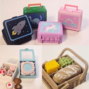 May include: A collection of miniature toy lunchboxes featuring rocket, dinosaur, unicorn, and rainbow designs, alongside small boxes containing miniature cake and pastry figures, and a picnic basket filled with bread, cheese, and grapes.