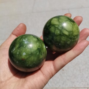 Peut inclure: Deux objets sphériques lisses en pierre verte polie avec une texture marbrée et tachetée, présentant des veines vert forêt foncé et vert citron plus clair sur toute la surface, avec une finition naturelle brillante et des formes arrondies.