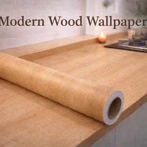 Puede incluir: Un rollo de papel pintado con vetas de madera marrón claro descansa sobre una encimera de madera. El texto "Modern Wood Wallpaper" se muestra encima del rollo. Se ve una vela encendida y una placa.