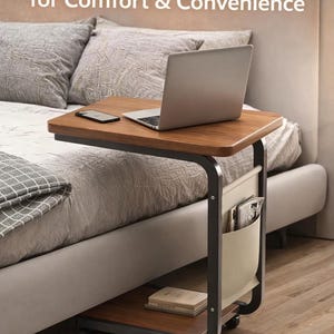 Könnte beinhalten: Ein rollender Nachttisch mit dunkler Holzmaserung, einem schwarzen Metallrahmen und einer beigefarbenen Stofftasche. Der Tisch trägt einen Laptop, ein Telefon und Zeitschriften. Der Text auf dem Bild lautet: "Bedside Table for Comfort & Convenience."