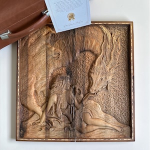 May include: A detailed wood carving depicting a mythical scene with figures and a dragon. The artwork is framed and accompanied by a certificate from Pasha Hand Art Gallery. The carving is in shades of brown.