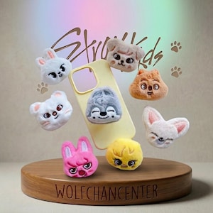 May include: A selection of plush animal phone grips, including a rabbit, dog, wolf, and chick, displayed around a yellow phone case. The background features the text "Stray Kids" and paw prints. The base reads "WOLFCHANCENTER".