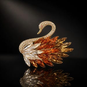 May include: A gold-toned swan brooch with a curved neck and a ruby eye. The swan's body is adorned with sparkling crystals in shades of white, orange, and gold. The brooch is set against a black background, with a mirrored reflection.