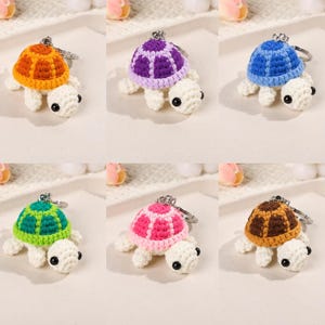 May include: A collection of six small, handmade crochet turtle keychains, each featuring a white body, black bead eyes, and a distinctively colored shell in orange, purple, blue, green, pink, or brown, attached to a silver metal keyring.