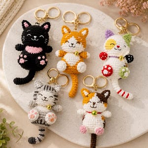 May include: Five crocheted cat keychains with gold-tone metal rings. The cats feature various colors including black with pink accents, orange and white, white with multi-colored patches, gray tabby stripes, and a white, brown, and orange calico pattern.