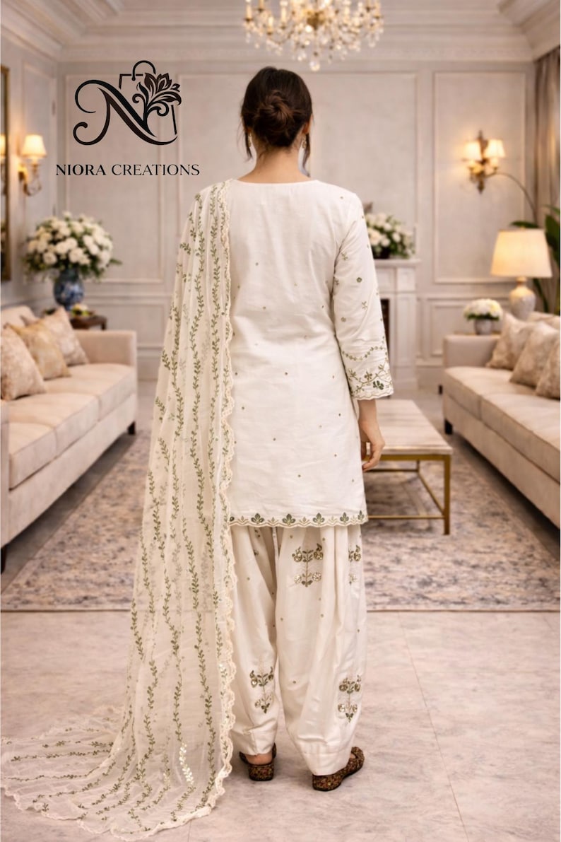 Puede incluir: Conjunto salwar kameez blanco con bordados intrincados. El atuendo incluye una t&uacute;nica, pantalones sueltos y una bufanda a juego. El bordado presenta patrones florales y de hojas en un color complementario. De Niora Creations.