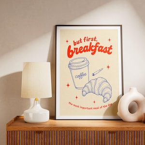 Peut inclure: Une affiche encadrée avec l'inscription "but first, breakfast" en rouge. L'affiche présente une tasse de café, un croissant et un petit objet, le tout en dessin au trait bleu. La phrase "the most important meal of the day" est en bas.