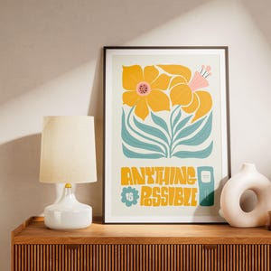 Peut inclure: Une affiche encadrée avec un motif floral et l'inscription "ANYTHING IS POSSIBLE" en jaune et turquoise. L'œuvre présente de grandes fleurs jaunes avec des accents roses et des feuilles turquoise. Une lampe blanche et des vases décoratifs sont posés sur une surface en bois.